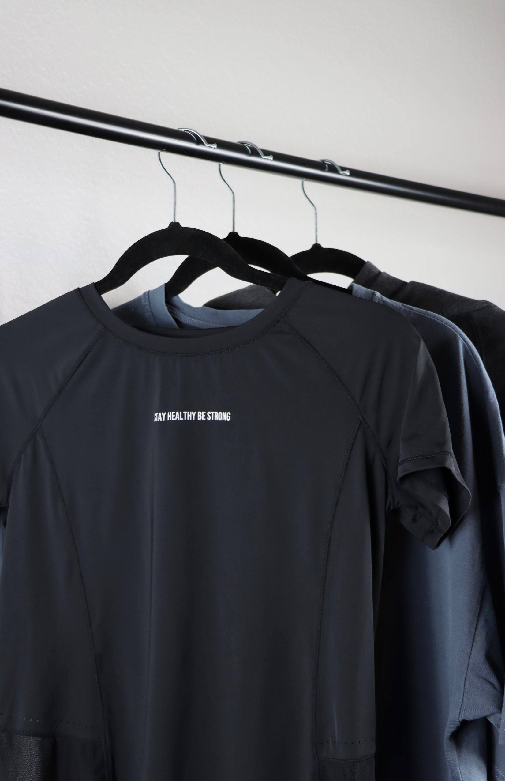 A black mesh t-shirt alongside a blue shirt and gray clothing is hung up